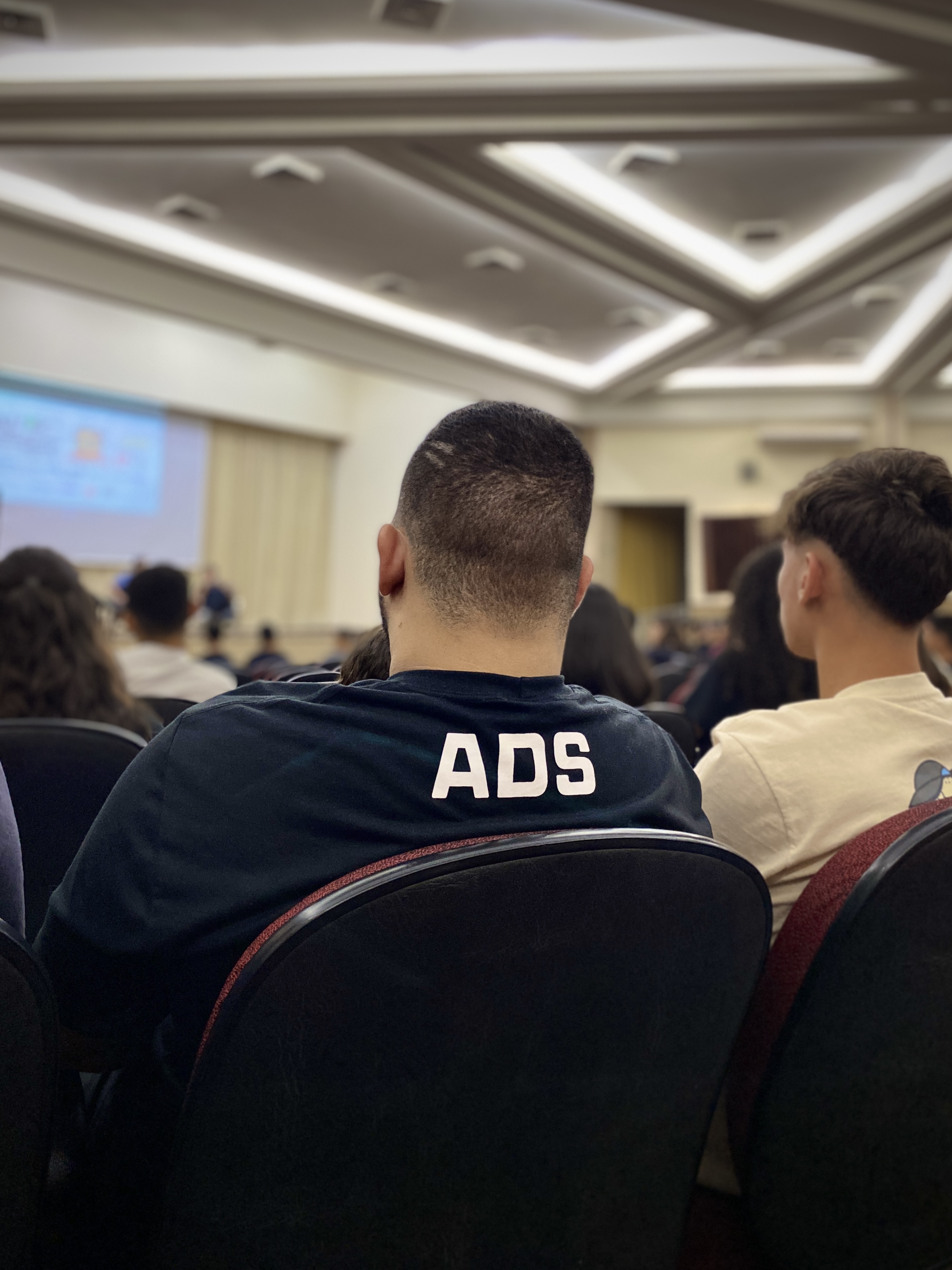 Participante com camiseta ADS assistindo apresentação sobre crescimento profissional
